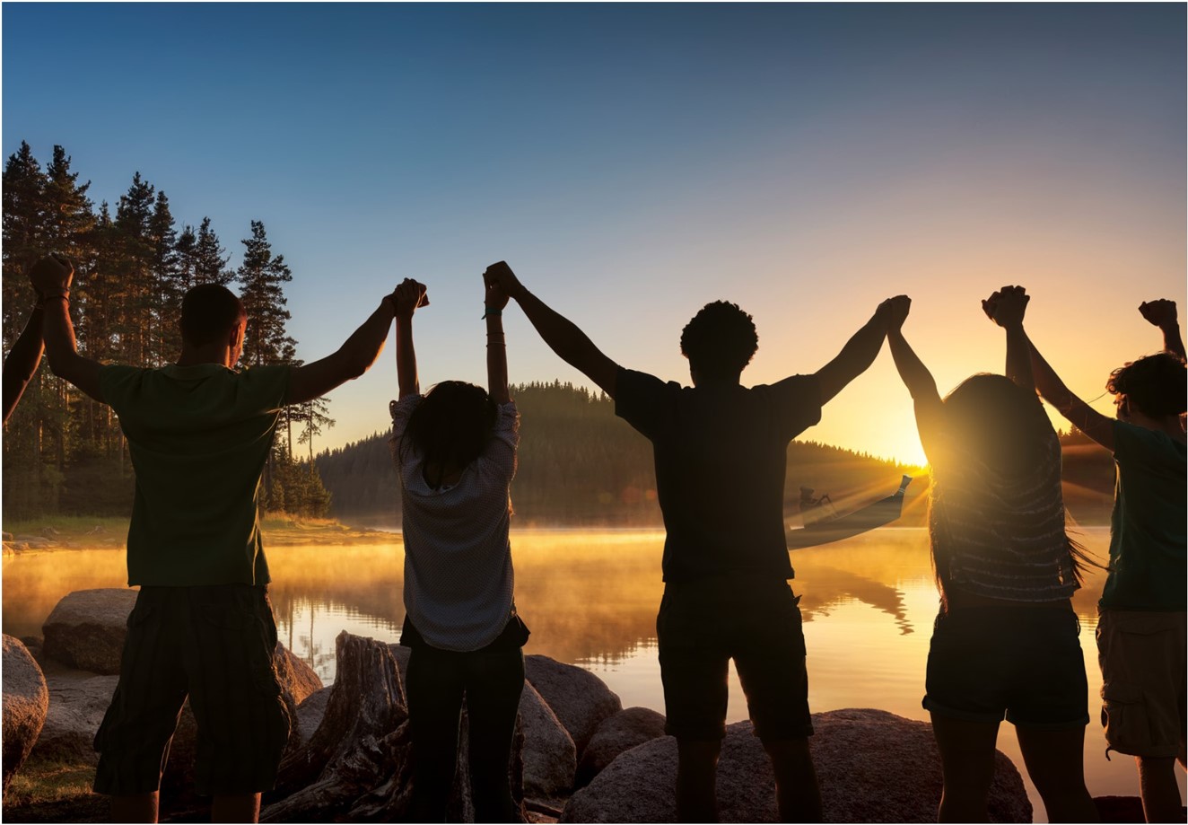 Groupe d’enfants les bras levés, se tenant par les mains et regardant un canot au coucher du soleil.