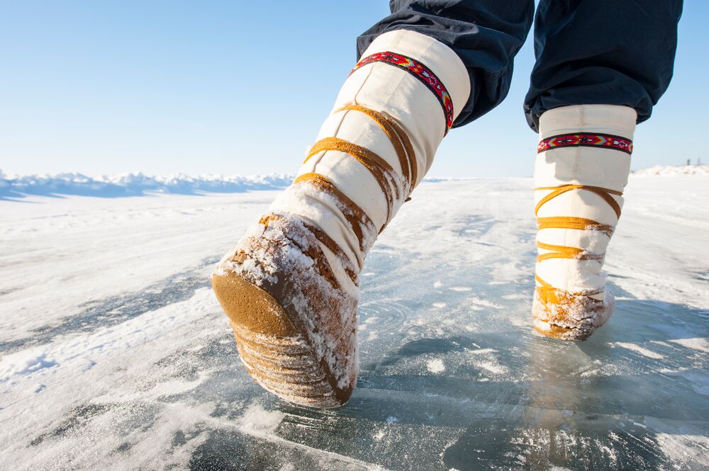 A person walks on ice in a pair of handmade boots with Indigenous designs at the top.