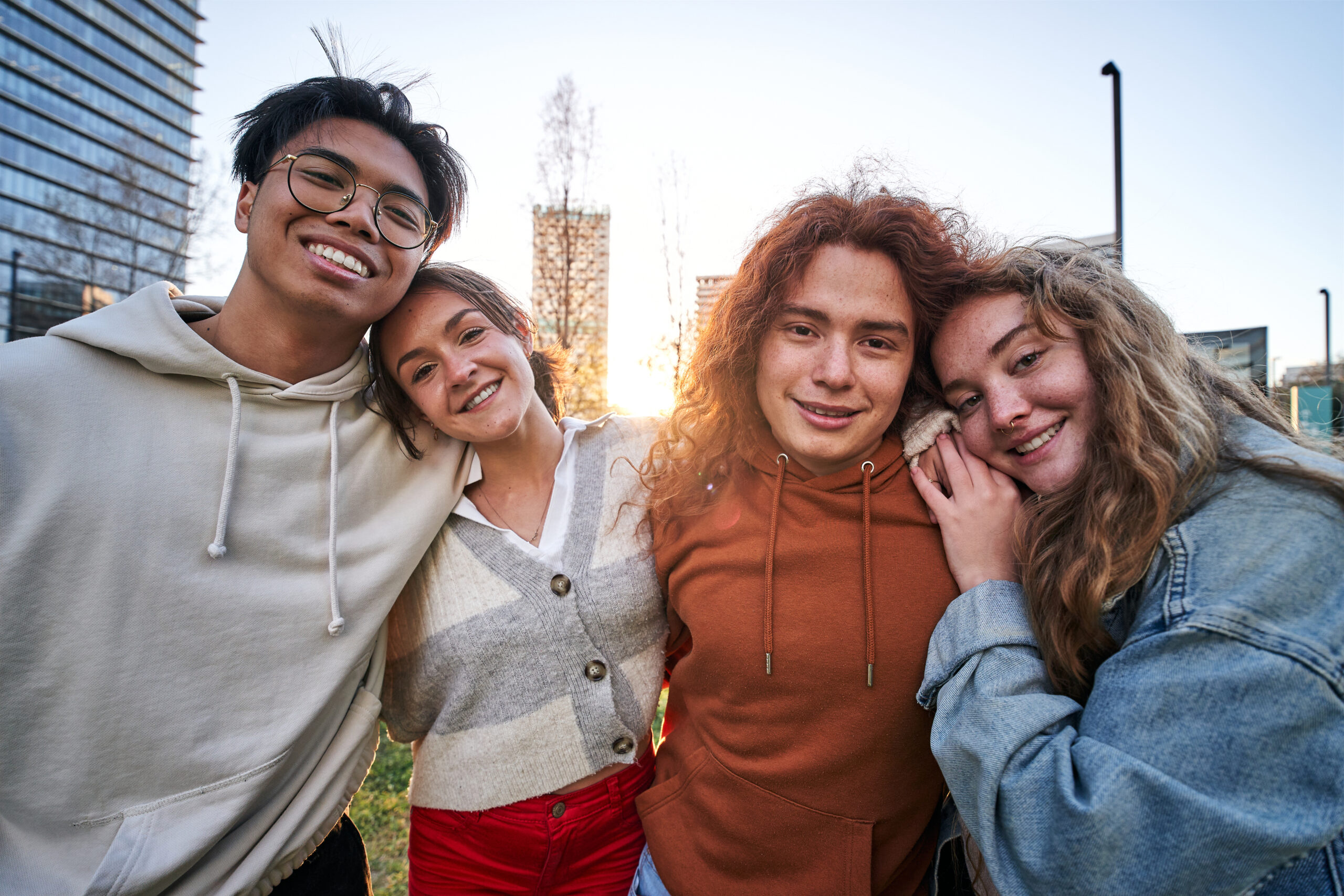 Portrait of a group of four students boys and girls having fun outdoors and they are hugging. The photo is taken outside the campus of the university. They look very happy and look at the camera.
