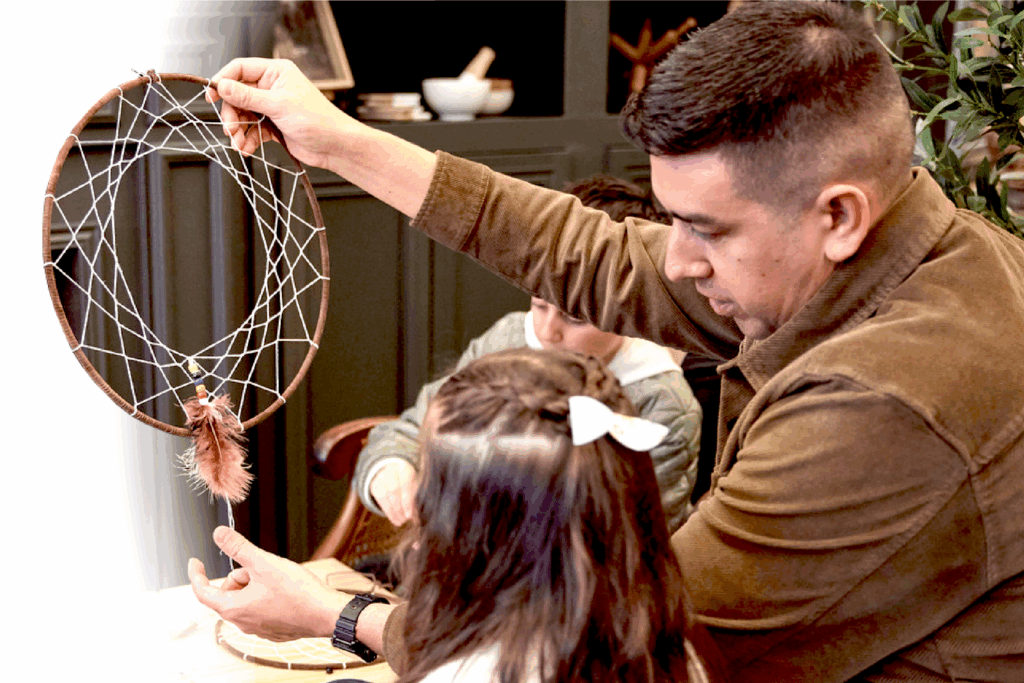 A Métis man with his daughter in their home holding a dream catcher