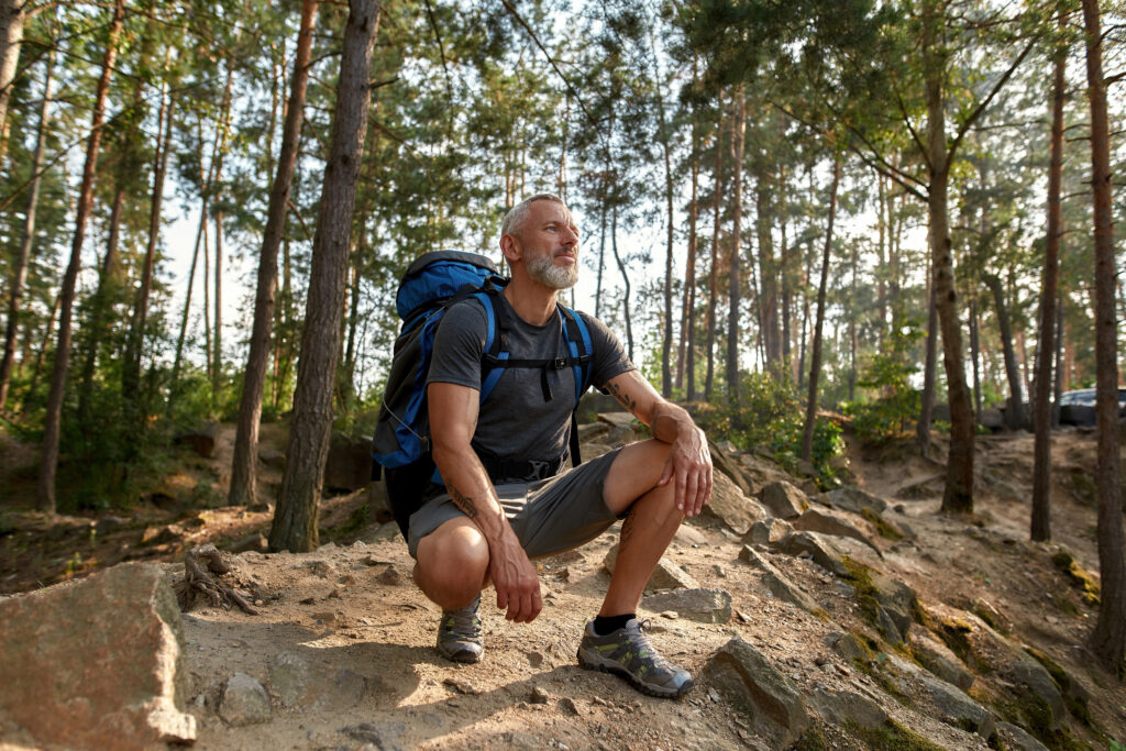 Middle aged man with backpack kneels while on a forest hike