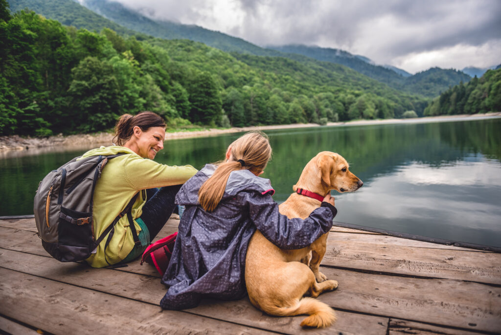 Mother and daughter with their dog on a hike by the waterfront of a forest