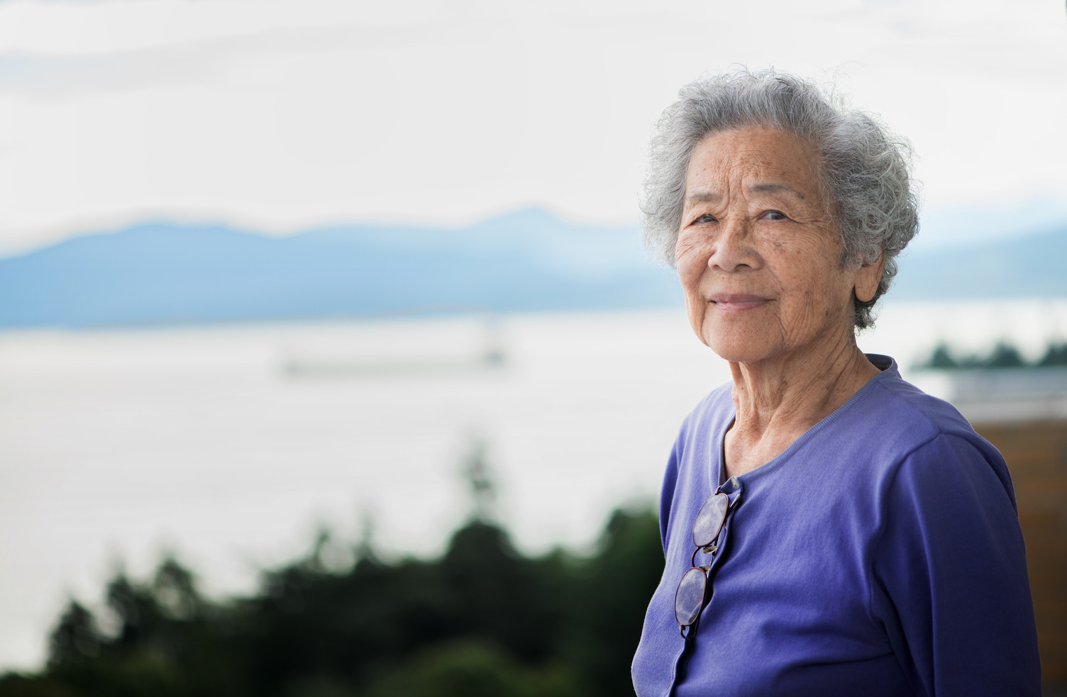 older adult standing outdoors near a waterfront landscape. 